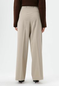 Beige broek met wijde pijpen en een hoge taille, voorzien van plooien, zijzakken en een gladde stoftextuur. Achteraanzicht van de taille naar beneden.