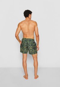 Herren-Badeshorts mit einem dunkelgrünen Grundton und aufwendigen gelb-grünen Blumenmustern, elastischem Bund und Seitentaschen.