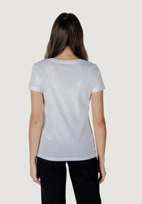 T-shirt in cotone bianco con maniche corte, scollatura rotonda e dettagli floreali delicati sul retro. Tessuto morbido, vestibilità casual.