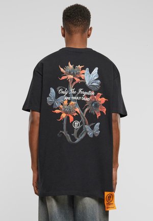Camiseta negra con gráficos coloridos de flores y mariposas en la parte posterior, con el texto "Solo los olvidados ESTÁN REALMENTE MUERTOS" y una etiqueta naranja.