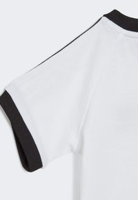 T-shirt bianco in cotone con colletto e bordi delle maniche a costine neri, texture liscia e maniche corte con rifiniture a contrasto lungo le cuciture delle spalle.