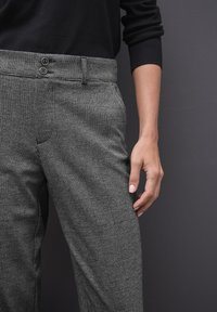Pantalons à carreaux gris avec un tissu texturé, dotés d'une taille haute, de deux boutons à la ceinture et de poches latérales.