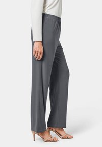 Grijze, wijde broek met elastische tailleband, gemaakt van een gladde stof, gecombineerd met lichtgekleurde sleehakken. Vlakke voorkant, geen zichtbare zakken.