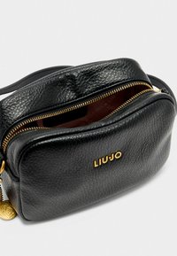 Borsa a tracolla in pelle nera con superficie texturizzata, hardware dorato, chiusura con zip superiore e nome del brand in rilievo sul fronte.