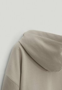 Light beige hooded sweatshirt showing the back and side seam with visible hood and soft, smooth fabric texture.