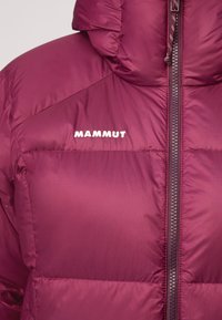 Bordowa kurtka puchowa z kapturem, z pełnym zamkiem błyskawicznym i haftowanym na białe logo "Mammut" na klatce piersiowej. Gładka tekstura.