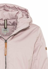 Světle růžová bunda s kapucí a zipovým zapínáním, se kontrastní šedou podšívkou, texturovanou nášivkou na rukávu a štítkem s logem uvnitř.