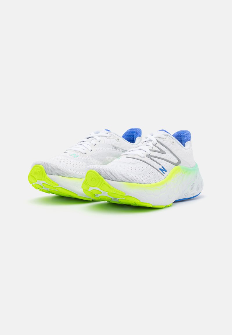 Un par de zapatillas de correr blancas con forro interior azul, logotipos grises y azules, y suelas verde neón sobre un fondo blanco.