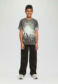 Graues T-Shirt mit kurzen Ärmeln und einem Grafikmotiv von erhobenen Händen, kombiniert mit schwarzen weiten Hosen und hellen Sneakers.