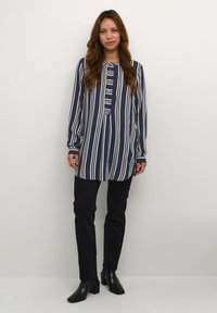 Camisa de rayas azul marino y blanca de manga larga con cuello abotonado y botones en el pecho, combinada con pantalones negros y botines.
