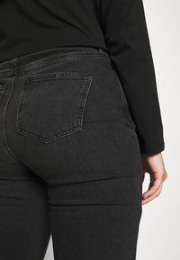 Jeans in denim nero dal taglio aderente, con due tasche posteriori, cuciture sottili e una texture liscia.