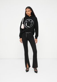 Czarna bluza z kapturem z srebrnym logo, w zestawieniu z czarnymi spodniami typu dzwony z bocznymi rozcięciami oraz czarnymi czółenkami. Uzupełniona różową torebką.