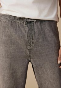 Pantaloni din denim gri cu o croială lejeră, având o talie elastică și o textură subtilă. Materialul are un aspect uzat, decolorat.