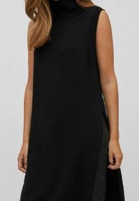 Svart ärmlös klänning med hög polokrage. Tillverkad av stickad tyg, med en lång, rak passform och sidoklyftor för rörelse.