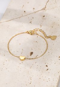 Pulsera de oro con un charm en forma de corazón, delicados eslabones de cadena y cierre de langosta con cadena de longitud ajustable.