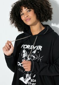 Zwarte hoodie met grafische print van een kat en tekst. Inclusief zilveren kettingdetail, lange mouwen en contrasterende stiknaden.