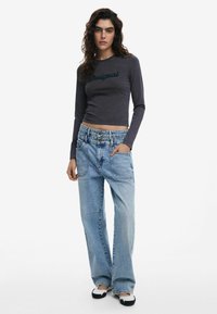 Dlhý rukáv šedého topu s logom "Desigual", skombinovaný s svetlomodrými džínsami s širokým strihom, ktoré majú dve predné vrecká a uvoľnený strih.