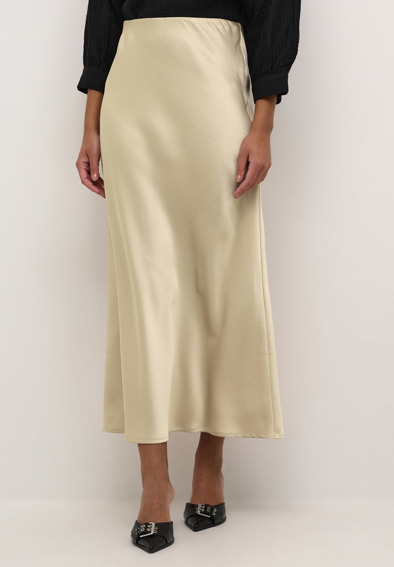 Satin beige maxinederdel med en glat tekstur, let udvidet design, sideslids og en taljeelastik. Sammen med sorte spidse sko.