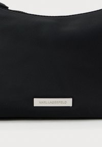 Pochette nera in nylon con una texture liscia e una placca logo argentata che riporta "KARL LAGERFELD" sul davanti. Design compatto per una facile portabilità.