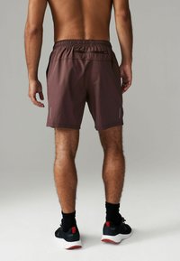 Brune sportshorts med snørelukning og reflekterende detaljer, parret med sorte sko og sokker, set bagfra.