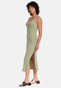 Grönrandig bodycon klänning med rundad halsringning, sidöppning och ribbad textur. Bärs med svarta och krämfärgade mules med en cirkulär detalj.