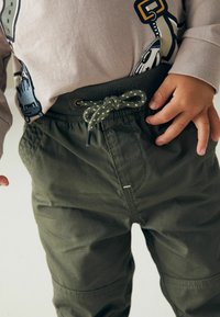 Pantalons vert olive avec une taille élastique et un cordon de serrage texturé. Comprend des poches et un tissu durable, adapté à un usage décontracté.