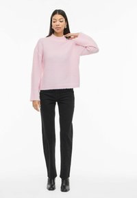 Jasnoróżowy sweter na drutach z wysokim kołnierzem i prążkowanymi długimi rękawami, zestawiony z czarnymi prostymi jeansami i czarnymi botkami za kostkę.