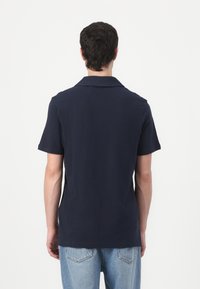 Mörkblå kortärmad polo med klassisk krage, tillverkad av mjukt bomullsmaterial, har rak skärning och minimal detaljer.