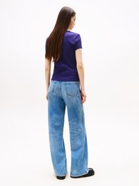 Tricou violet, ajustat, cu mâneci scurte, asortat cu blugi largi, de culoare albastră deschisă. Textură netedă a denimului, detalii minime și încălțăminte neagră.