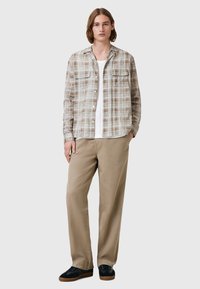 Rutig skjorta i beige och bruna toner, tillverkad i lätt tyg, har två bröstfickor. Matchad med beiga byxor och svarta sneakers.