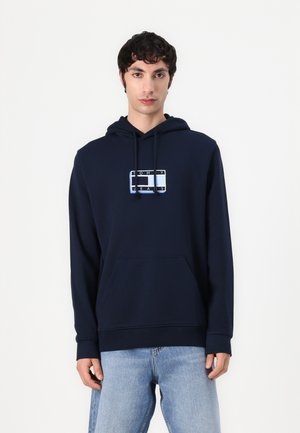 Sudadera azul marino de mezcla de algodón con un bolsillo frontal y capucha con cordón. Presenta un logotipo gráfico en blanco y azul claro.