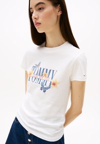 Witte katoenen t-shirt met een kleurrijke grafische print van bloemen en vlinders, met de tekst "TOMMY JEANS NEW YORK", ronde hals en korte mouwen.