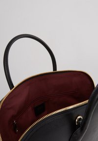 Czarna skórzana torebka na ramię ze złotym zamkiem, teksturowanym wykończeniem i burgundowym wnętrzem. Posiada kieszeń na zamek błyskawiczny oraz okrągłe uchwyty.