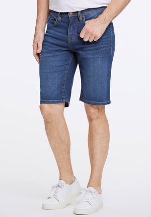 Shorts en denim bleu foncé avec une coupe droite, un design à cinq poches et des détails de couture subtils. Associés à des baskets blanches.