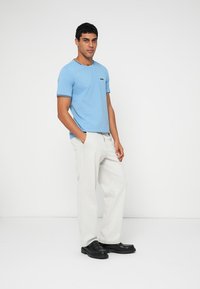 Light blue cotton t-shirt with a crew neck and black logo, paired with beige wide-leg pants and black shoes. Simple design, smooth texture.