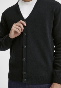 Svart ull cardigan med V-hals-design, med seks svarte knapper foran og ribbestrikket kant og mansjetter for tekstur.