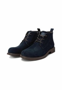 Botas de tobillo de ante azul marino con cordones marrones, suela marrón cosida y una lengüeta para facilitar su uso. Cuenta con un diseño de punta redonda.