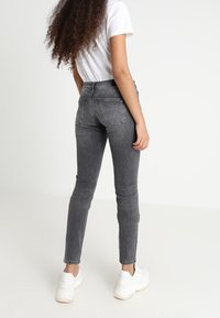 Vaqueros de mezclilla gris con cintura alta, corte ajustado y detalles de costura sutiles. Combinados con una camiseta blanca y zapatillas blancas.
