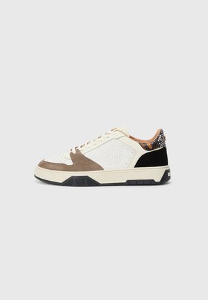 Lågklackade sneakers i beige, brun mocka och svarta detaljer, med präglad logotyp på sidan och ormskinnsmönster på hälkragen.