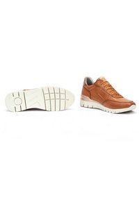 Zapatillas de cuero marrón con suelas de goma blanca, que presentan puntas redondeadas, paneles texturizados y cordones prominentes. Se muestran vistas de perfil y de la parte inferior.