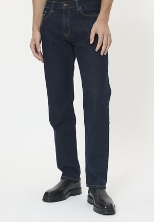 Dunkelblaue Denim-Jeans mit geradem Schnitt, ausgestattet mit Taschen und Kontrastnähten. Getragen mit schwarzen Lederstiefeln.