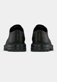 Ténis em pele preta com textura suave, apresentados com sola grossa preta e detalhes do logótipo em relevo no calcanhar. Design minimalista.