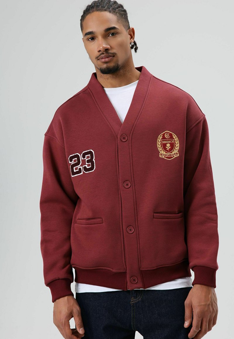 Bordeauxrood vest met sjaalkraag, geborduurd logo, knoopsluiting en twee steekzakken; gemaakt van zachte, gestructureerde stof.