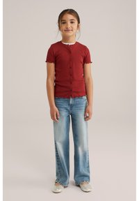 Top rosso a coste con bottoni e maniche corte, bordi scallop; jeans svasati azzurro chiaro; ballerine argentate scintillanti.