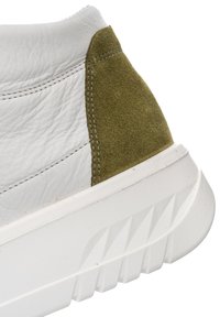 White leather shoe heel with olive green suede patch and thick white sole featuring geometric tread pattern.