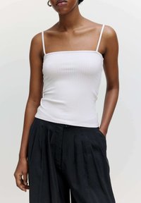Witte geribbelde tanktop met dunne bandjes, gecombineerd met zwarte geplooide broeken. De top heeft een aansluitend ontwerp en een gladde textuur.