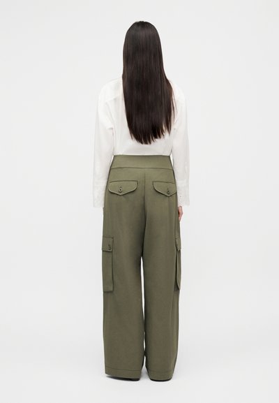 Pantalon cargo vert olive à jambes larges, deux poches avant et taille haute, associé à une chemise blanche à manches longues ornée de détails en dentelle.