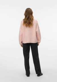 Roze gebreide trui met een gestructureerde afwerking, oversized pasvorm en brede mouwen, gecombineerd met zwarte broeken en zwarte schoenen.