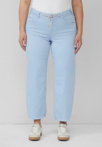 Jasnoniebieskie dżinsowe spodnie typu wide-leg, z elastycznym paskiem, przednimi kieszeniami i wykończeniem z frędzlami. Zestawione z białymi trampkami.