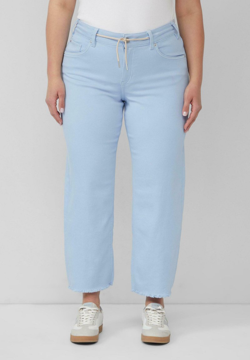 Jasnoniebieskie dżinsowe spodnie typu wide-leg, z elastycznym paskiem, przednimi kieszeniami i wykończeniem z frędzlami. Zestawione z białymi trampkami.